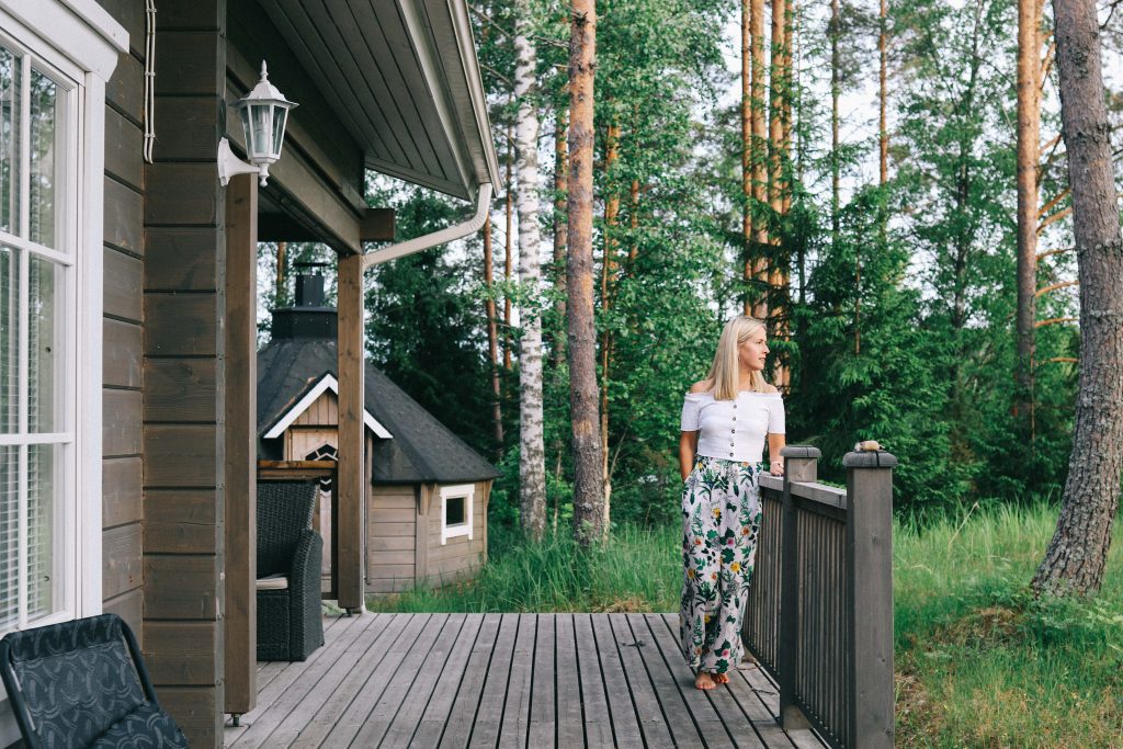 A girl stood on the veranda of a log cabin, in a woodland in Tampere.