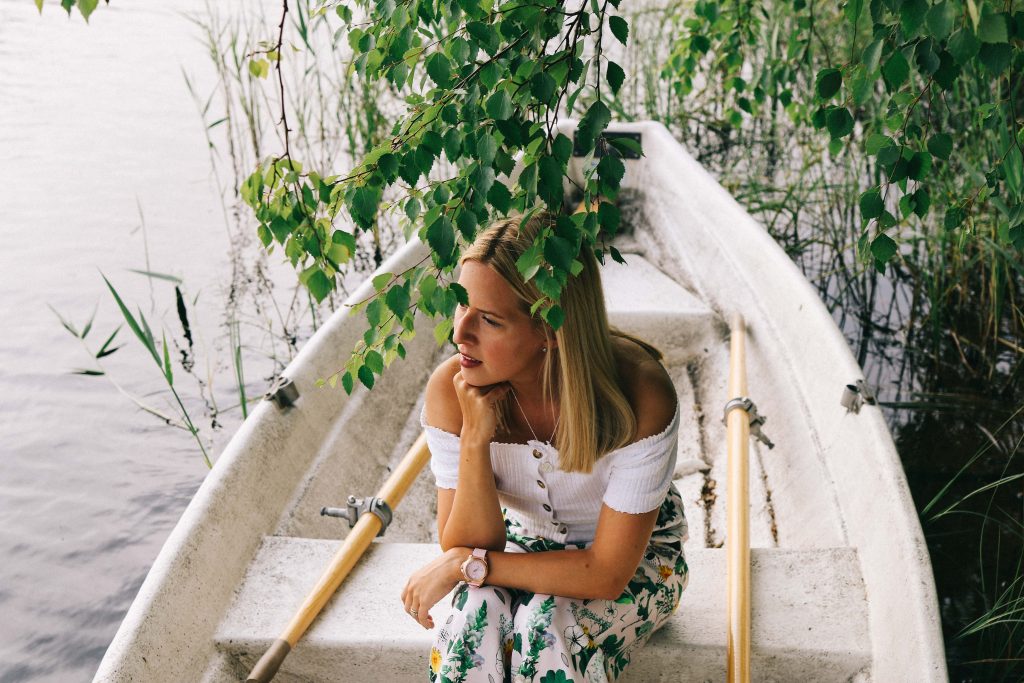 A girl sits in a small white row boat on a Finnish lake. Surrounded by green trees.