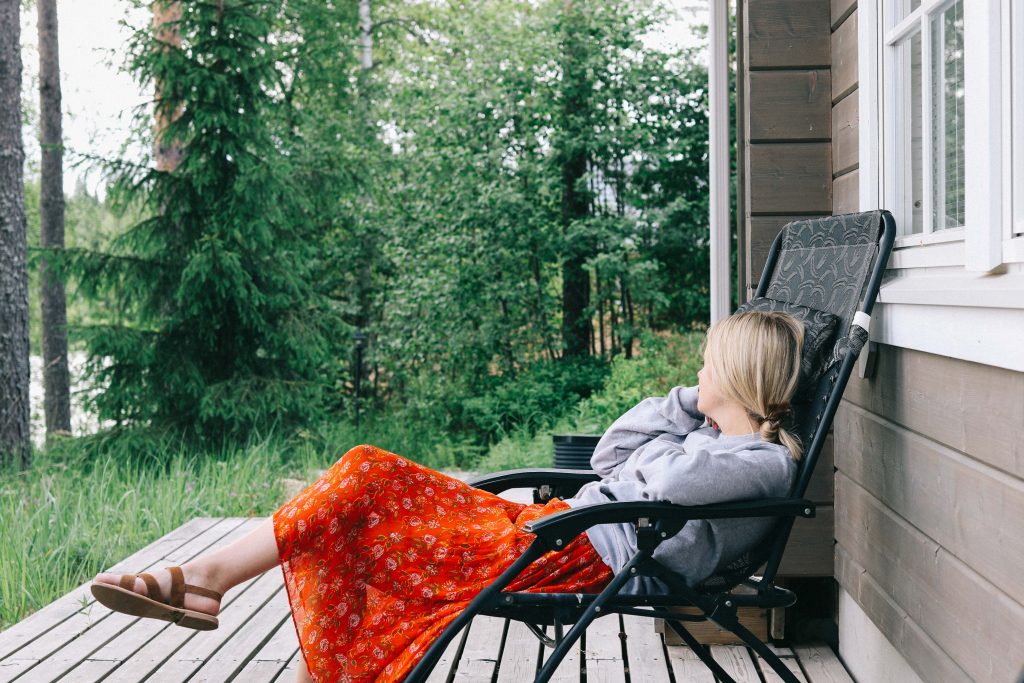 A girl reclining in a chair on the deck of a log cabin in Tampere.