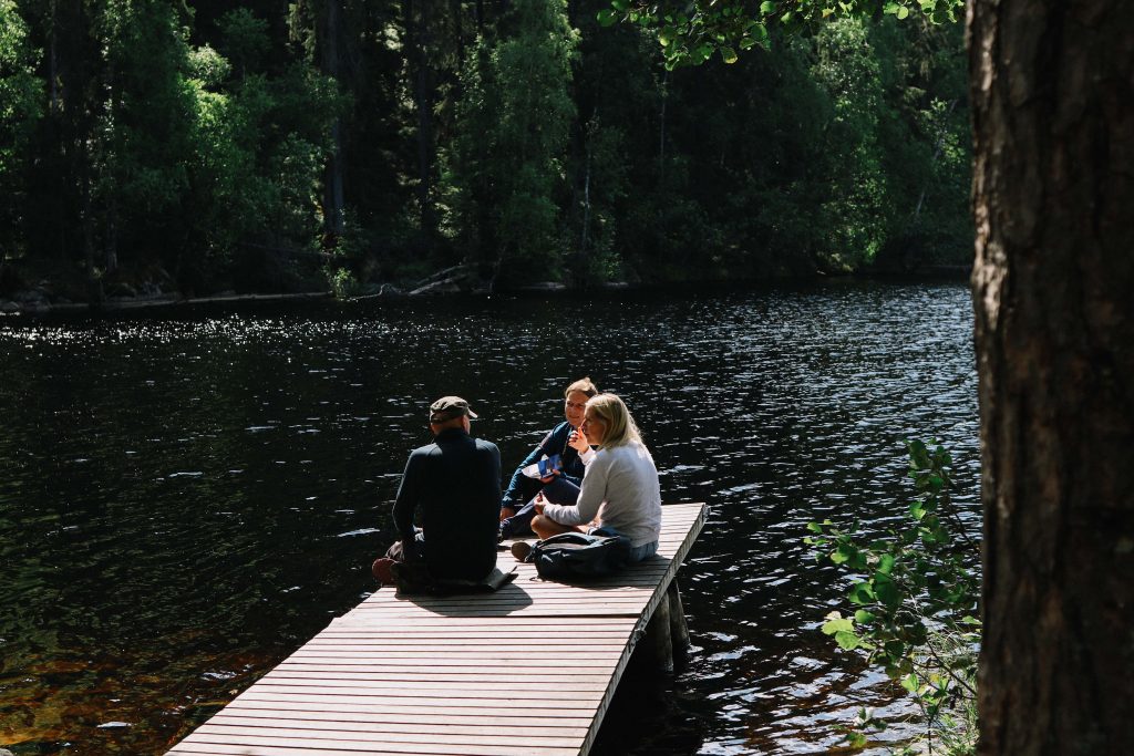 A group of three hikers have lunch on a jetty overlooking a lake in Helvetinjärvi National Park.